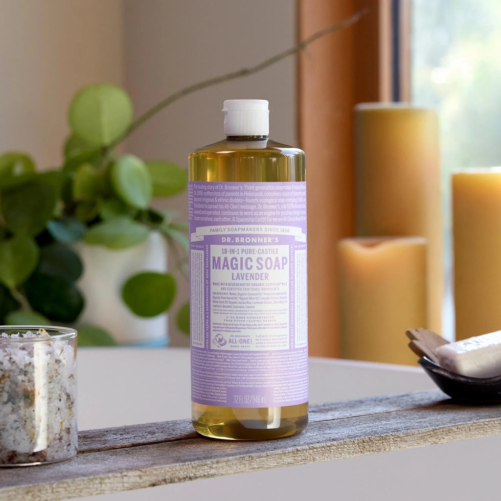 A bottle of Dr. Bronners 18 in 1 Pure Castile Magic Soap in lavender scent stands on a rustic board in a cozy room with candles and greenery, featuring 32 fl oz capacity [32 oz]