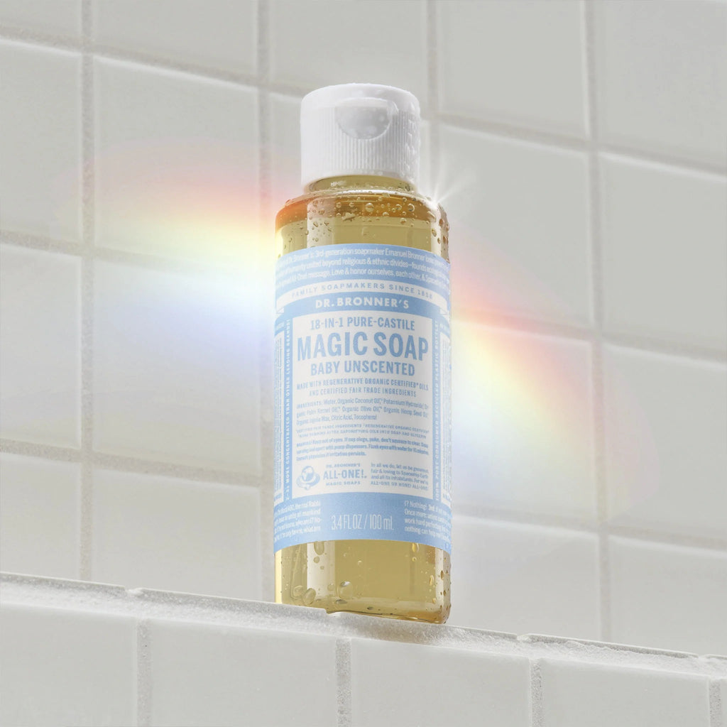Dr. Bronners 3 in 1 Pure Castile Magic Soap, Baby Unscented version, sits on a white tiled surface, with a light rainbow reflection on the left, highlighting its eco friendly packaging [3.4 oz]