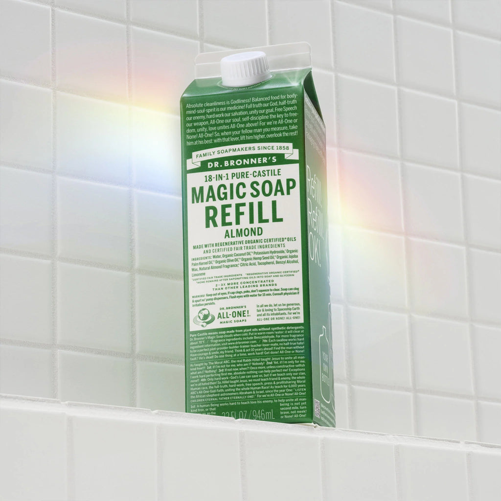 Dr. Bronners 18 in 1 Pure Castile Magic Soap Refill, Almond, rests on white tiled surface, exhibiting natural soaps eco friendly packaging. Text highlights Made with regenerative organic certified oils and certified fair trade ingredients [32 oz]