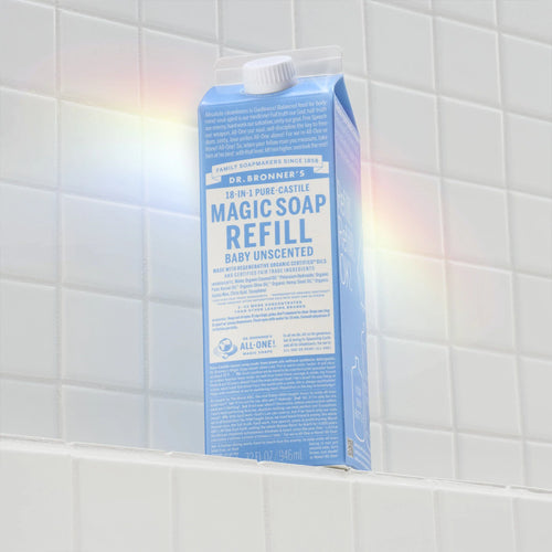 Carton of Dr. Bronners 18 in 1 Pure Castile Magic Soap Refill sits on white tiled shelf, text highlighting organic, eco friendly uses, and sustainability benefits under soft lighting [32 oz]