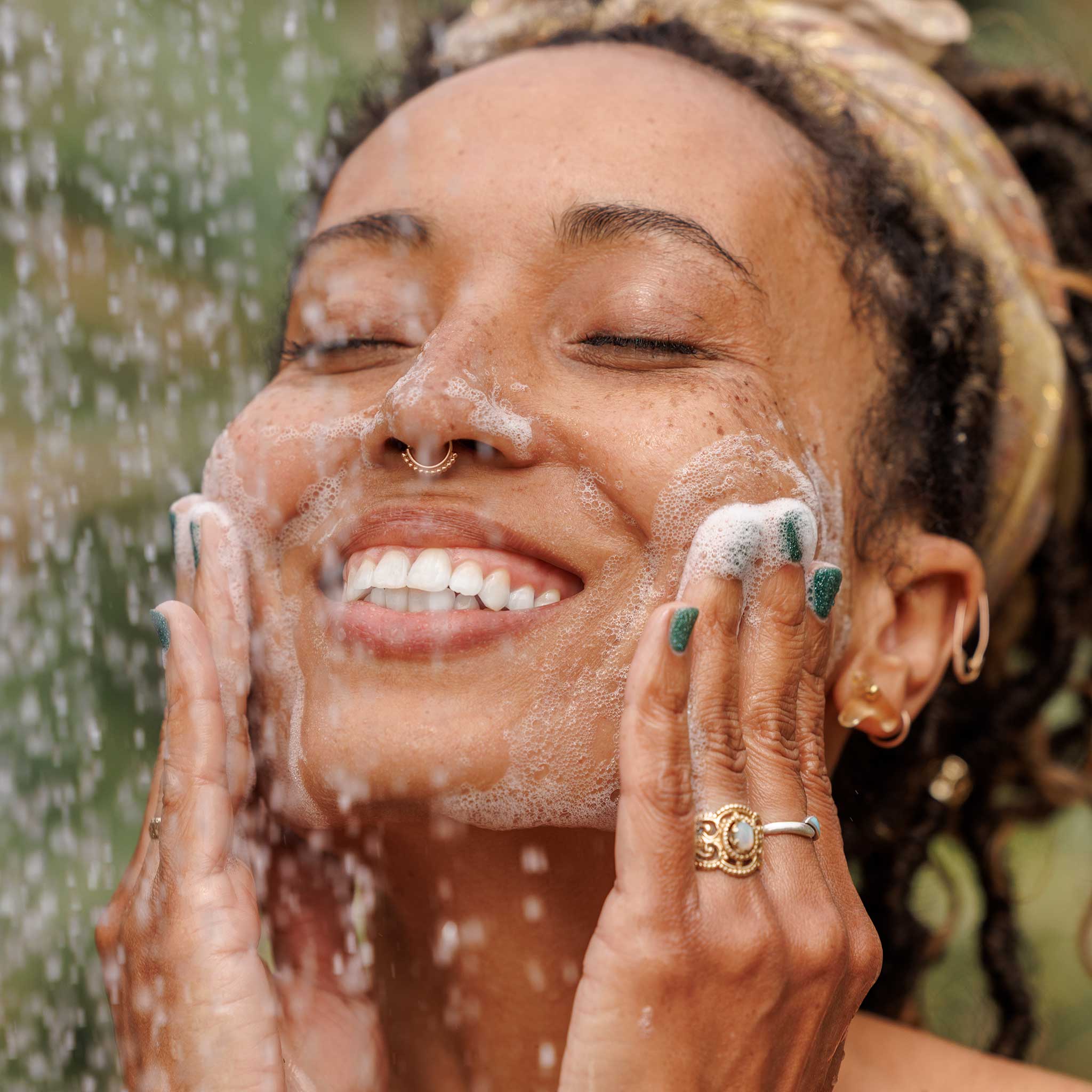 A person joyfully washes their face with soapy bubbles, using liquid castile soap, under a shower. They are outside, with greenery in the background, showcasing eco friendly skincare in a natural setting  [32 oz]